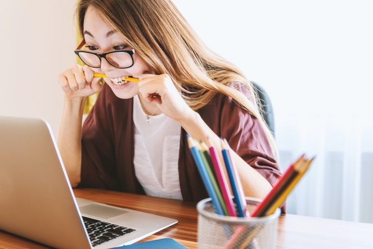 woman biting pencil sitting in front of laptop on daytime