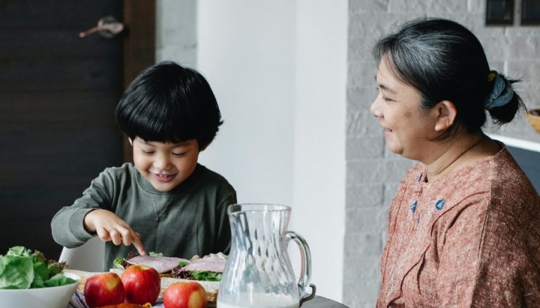 A boy eating happily with his mother.